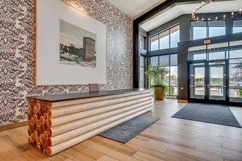 a large glass door opens to a hallway with a wood reception desk and a painting on the